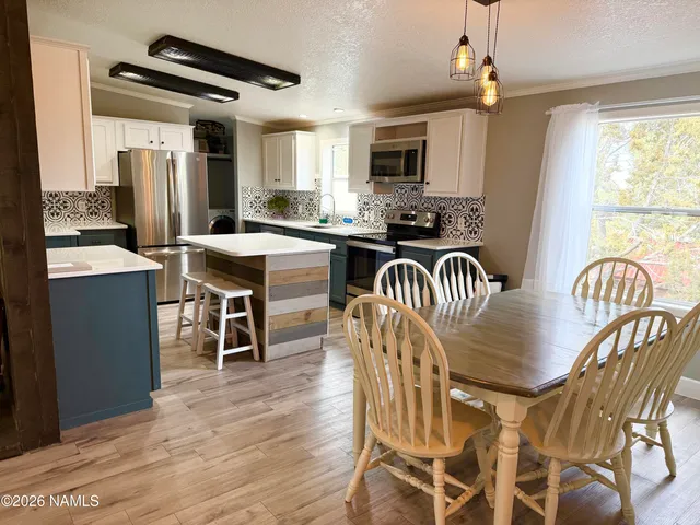 a kitchen with stainless steel appliances granite countertop a stove a refrigerator a microwave a dining table and chairs with wooden floor