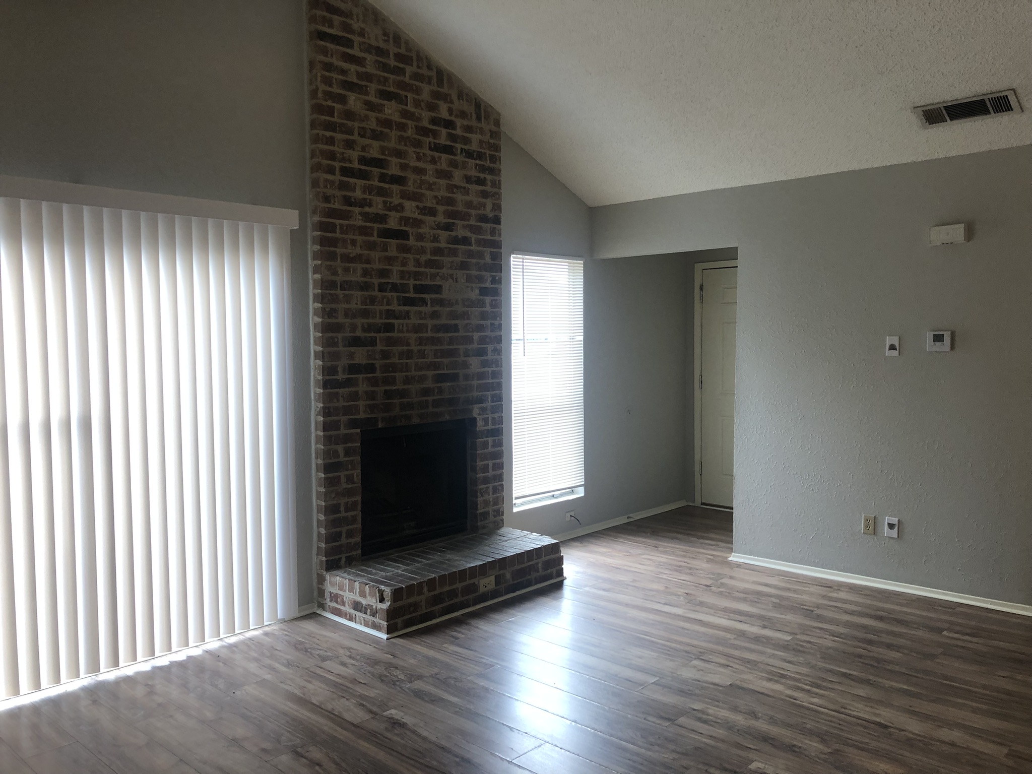7002 Ivory Key Court, Unit B Austin, TX 78745 - Photo 3 of 10 Unfurnished living room with a brick fireplace, dark wood-style flooring, vaulted ceiling, a textured ceiling, and a textured wall
