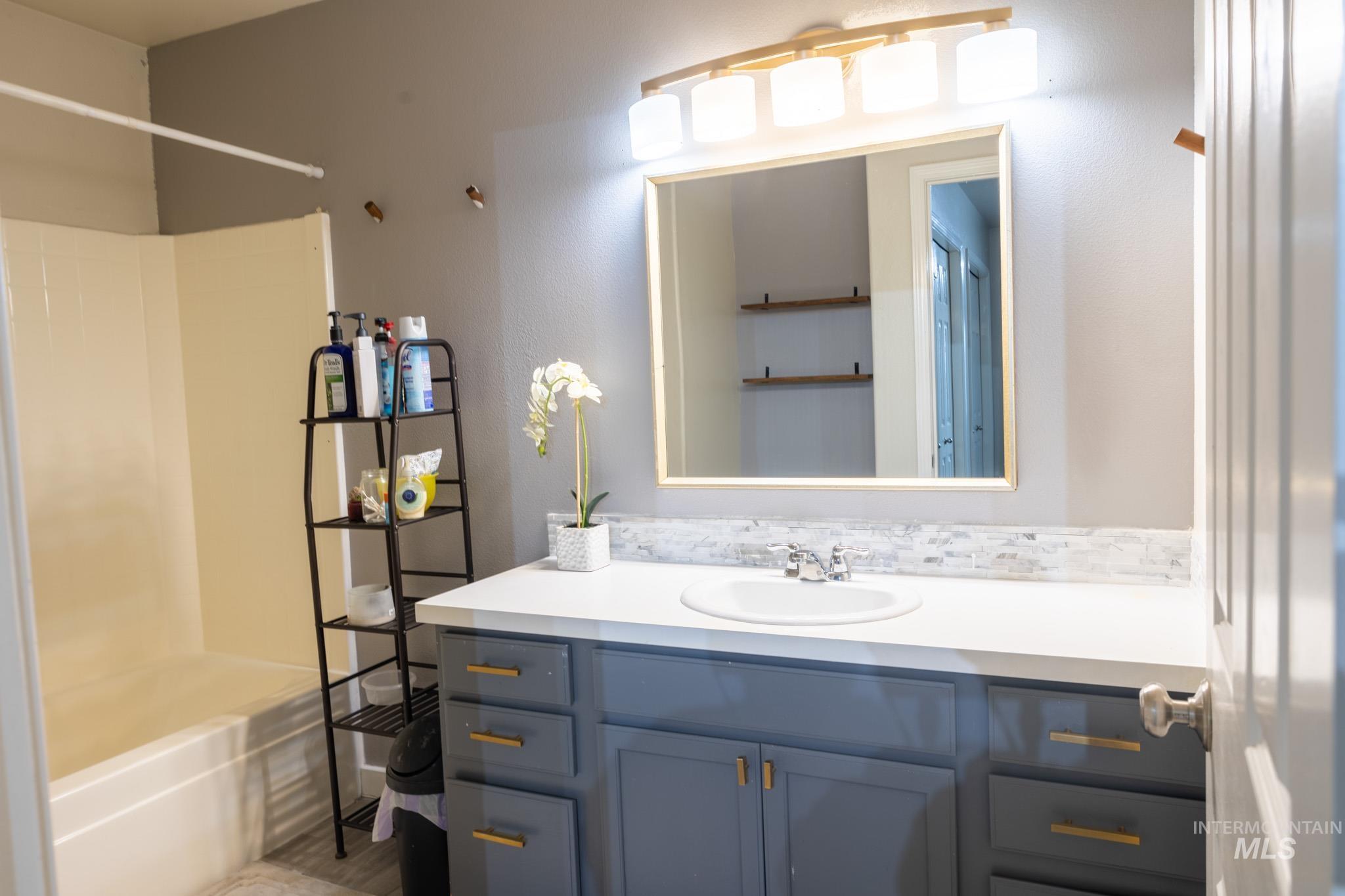 14409 Raleigh Court Caldwell, ID 83607 - Photo 8 of 15 White solid-surface countertop with an integrated sink, mosaic tile backsplash, and a gold-framed wall mirror