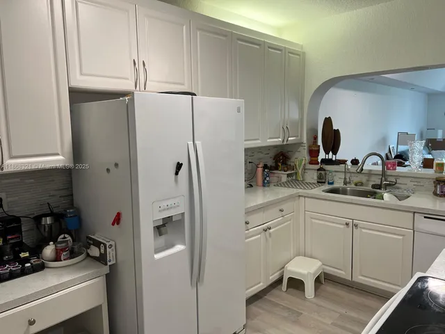 a kitchen with a sink dishwasher and white cabinets with wooden floor