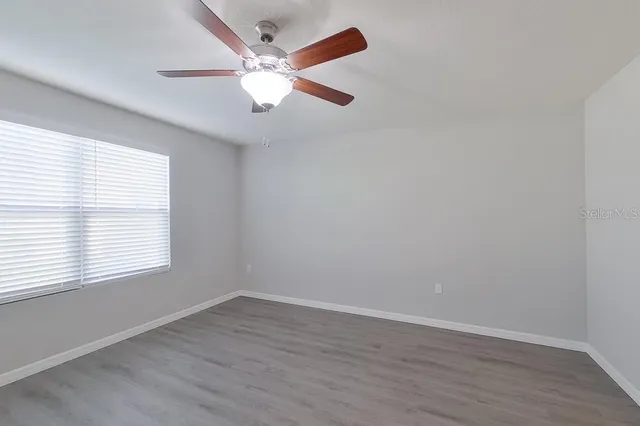 an empty room with wooden floor fan and windows