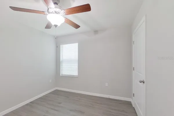 an empty room with wooden floor fan and windows