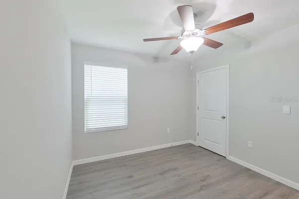 an empty room with wooden floor fan and windows