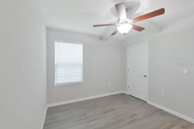 an empty room with wooden floor fan and windows