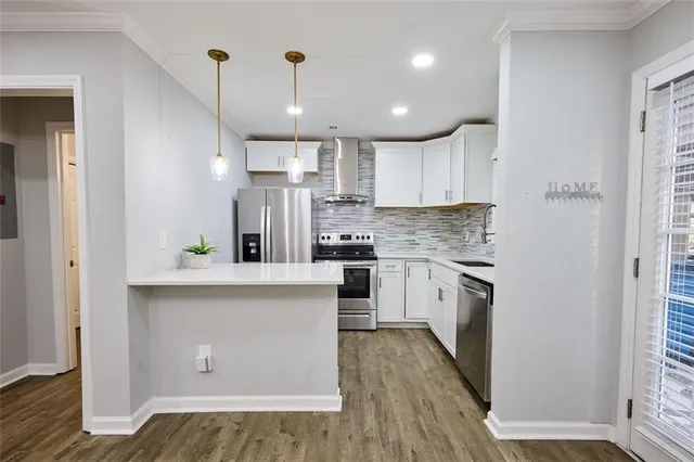 a kitchen with stainless steel appliances granite countertop a refrigerator a sink dishwasher a stove and white countertops with wooden floor