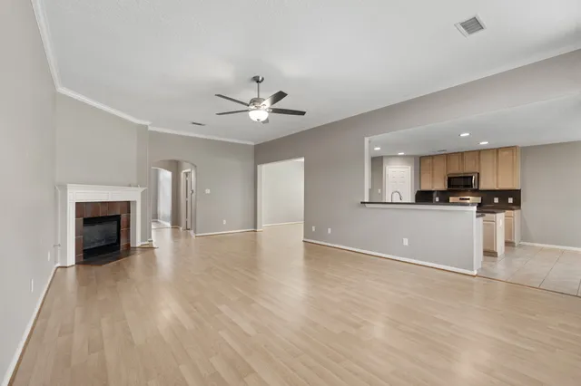 a view of an empty room and kitchen with wooden floor