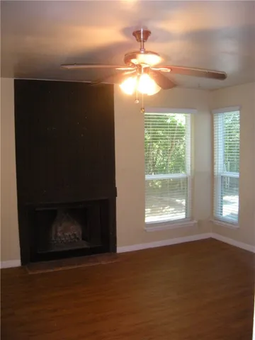 a view of an empty room with wooden floor fireplace and a window