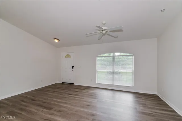 an empty room with wooden floor fan and windows