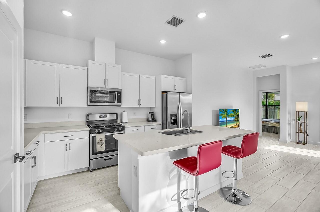 19567 Weathervane Way Loxahatchee, FL 33470 - Photo 7 of 49 a kitchen with stainless steel appliances kitchen island granite countertop a dining table chairs stove and white cabinets