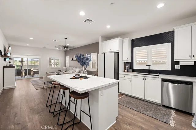 a kitchen with stainless steel appliances kitchen island granite countertop a sink a stove a refrigerator and island with wooden floor