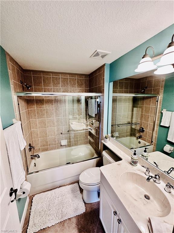 16152 Parque Lane Naples, FL 34110 - Photo 25 of 49 Full guest bathroom featuring vanity, tile patterned floors, combined bath / shower with glass door, toilet, and a textured ceiling
