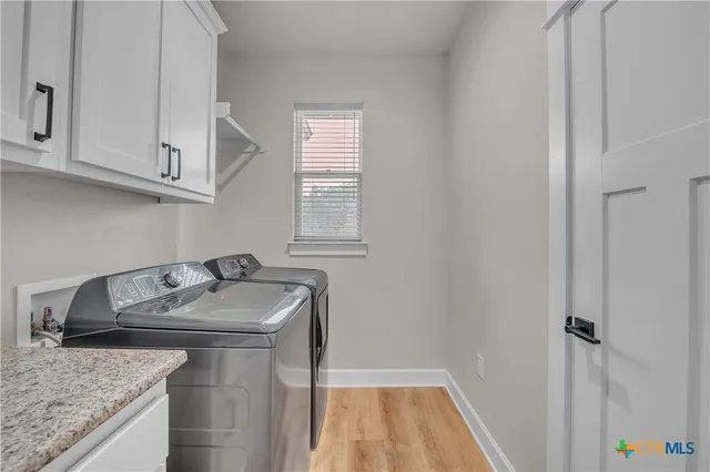 a bathroom with a granite countertop sink and washing machine with white cabinets