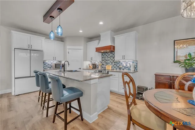 a kitchen with stainless steel appliances granite countertop a dining table chairs and a refrigerator