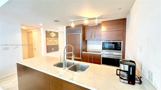 a living room with stainless steel appliances kitchen island granite countertop a sink and a large mirror next to a window
