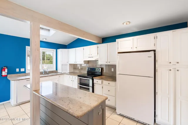 a kitchen with granite countertop a refrigerator a stove a sink and white cabinets with wooden floor