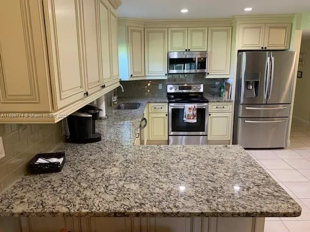 a kitchen with stainless steel appliances granite countertop a stove a refrigerator a sink a microwave and white cabinets