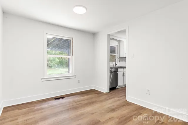 an empty room with wooden floor and a kitchen