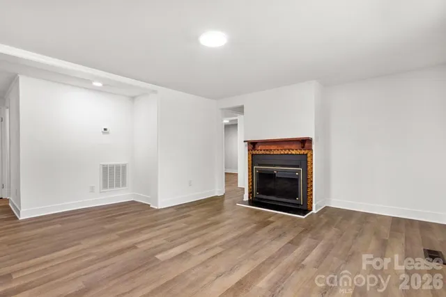 a view of an empty room with wooden floor fireplace and a window