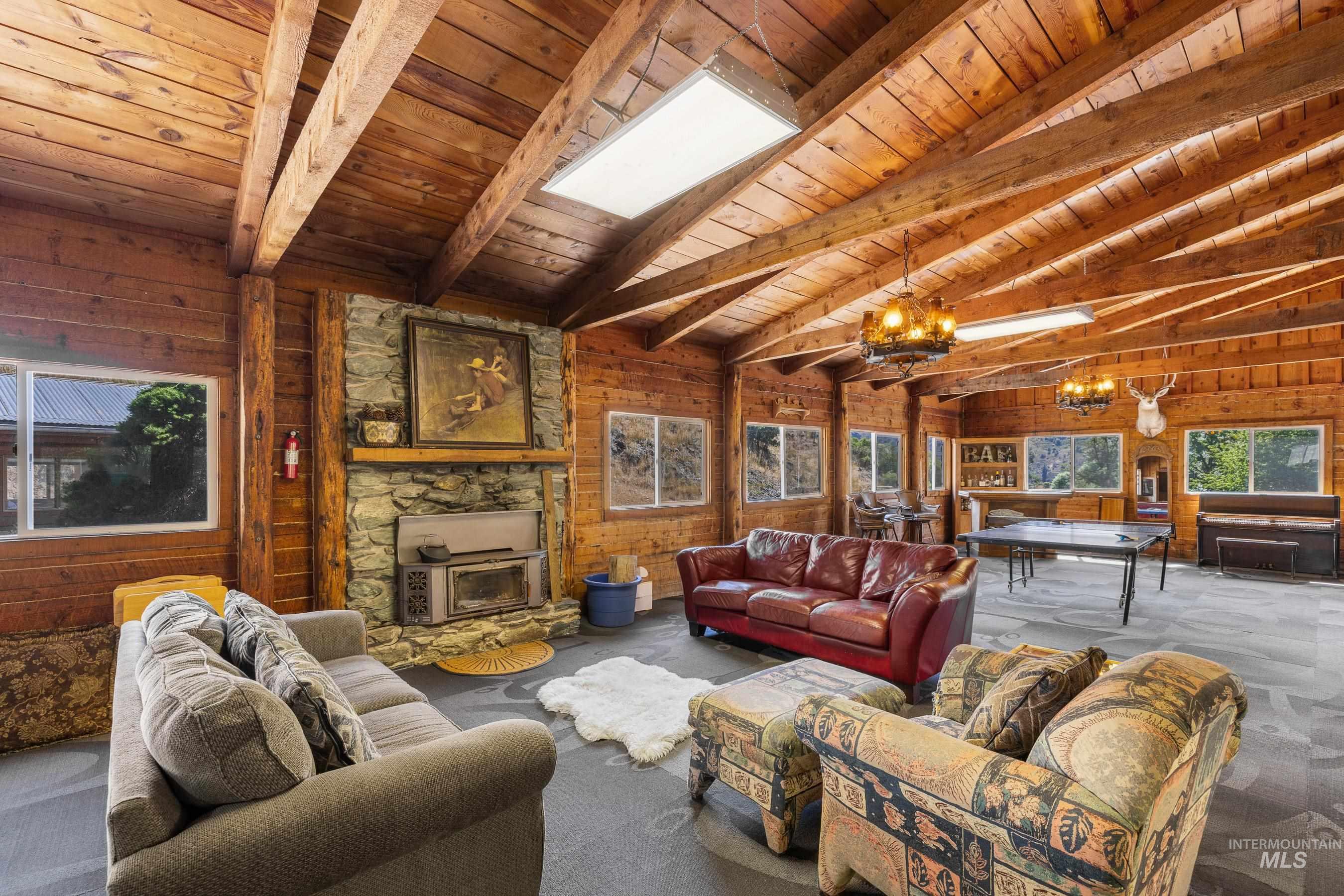 192 East Shingle Creek Road Riggins, ID 83549 - Photo 12 of 50 Living room featuring a chandelier, wood walls, a wood stove, carpet, and wooden ceiling