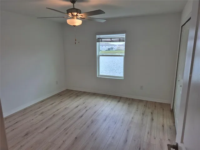 an empty room with wooden floor chandelier fan and windows
