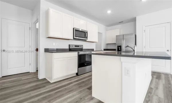 a view of kitchen and empty room with wooden floor