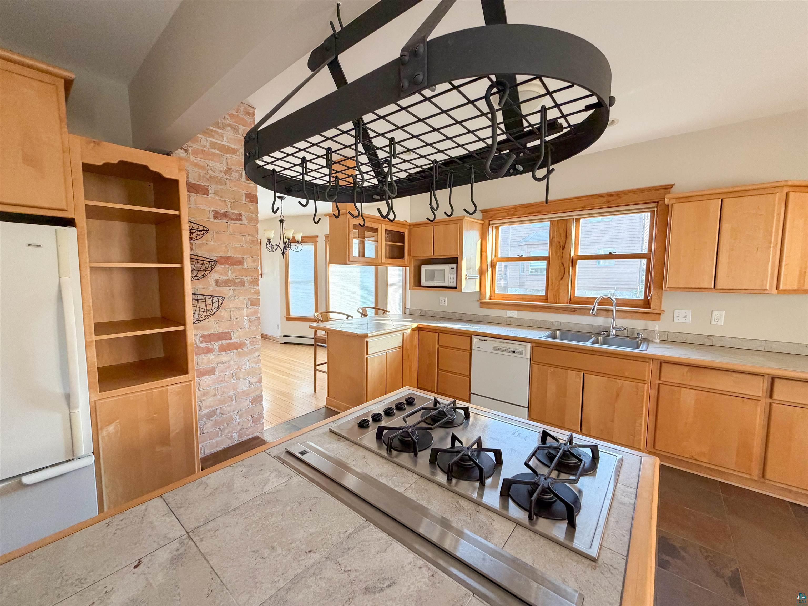 13 West 8th Street Duluth, MN 55806 - Photo 10 of 57 Kitchen featuring a central island with a built-in cooktop, light wood cabinetry, stone-finish countertops, and a double basin sink