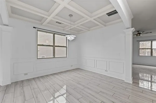 an empty room with wooden floor chandelier and windows