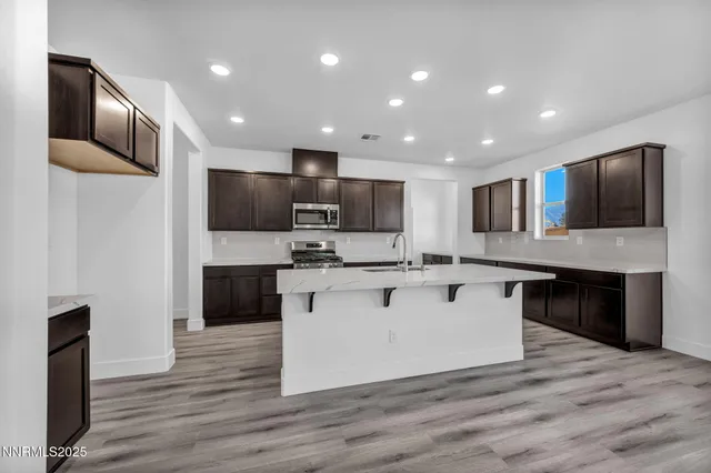 a large kitchen with stainless steel appliances kitchen island a sink dishwasher a refrigerator and a microwave oven with wooden floor