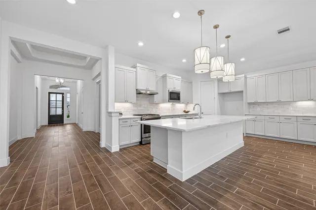 a large white kitchen with kitchen island a stove a sink dishwasher and white cabinets with wooden floor