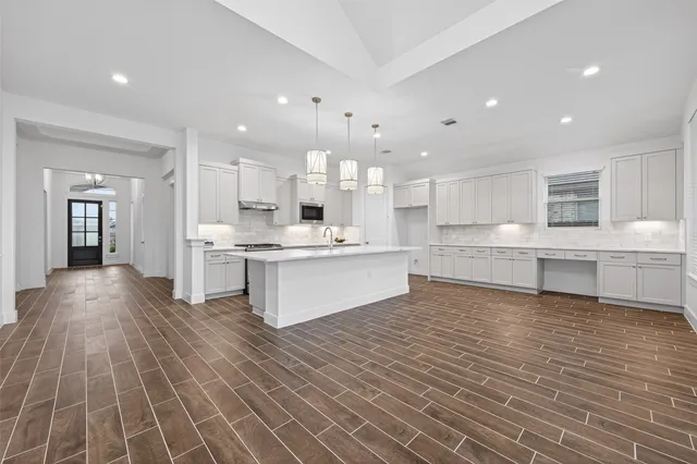 a large white kitchen with kitchen island a sink a stove a refrigerator and white cabinets with wooden floor