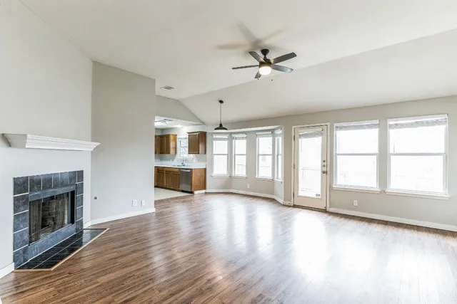 a view of an empty room with wooden floor fireplace and a window