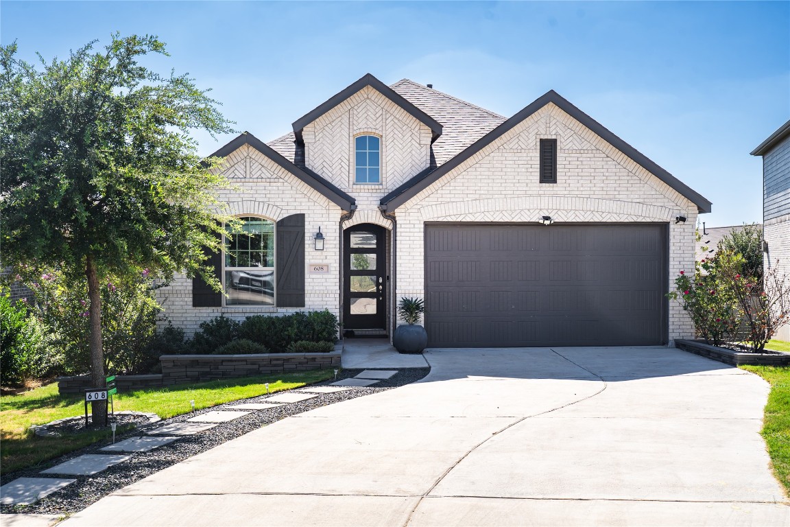 French country inspired facade featuring brick siding, concrete driveway, and an attached garage