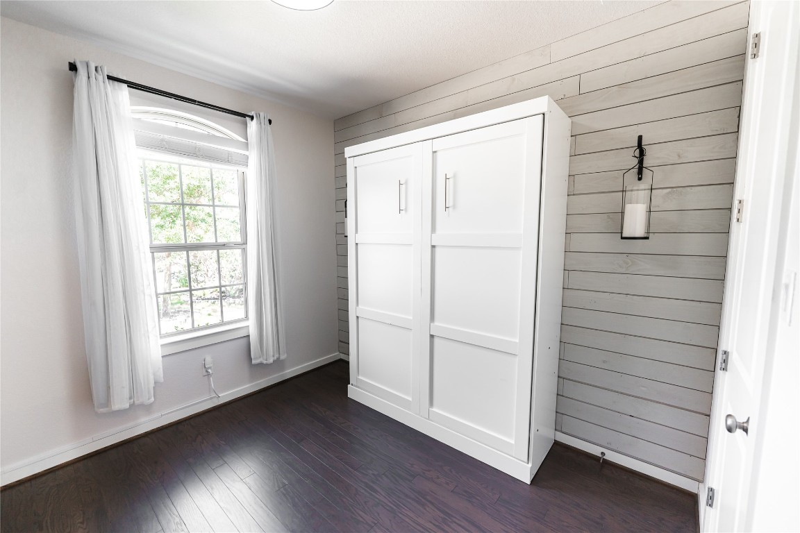 608 Pecan Bottom Trail Georgetown, TX 78628 - Photo 19 of 30 Unfurnished bedroom featuring dark wood finished floors, wood walls, and a closet