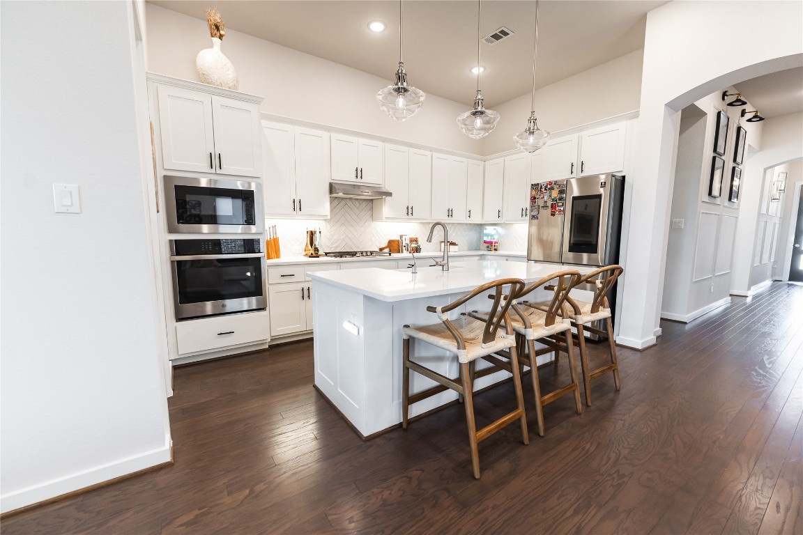 608 Pecan Bottom Trail Georgetown, TX 78628 - Photo 5 of 30 Kitchen featuring backsplash, arched walkways, dark wood-style flooring, stainless steel appliances, and pendant lighting