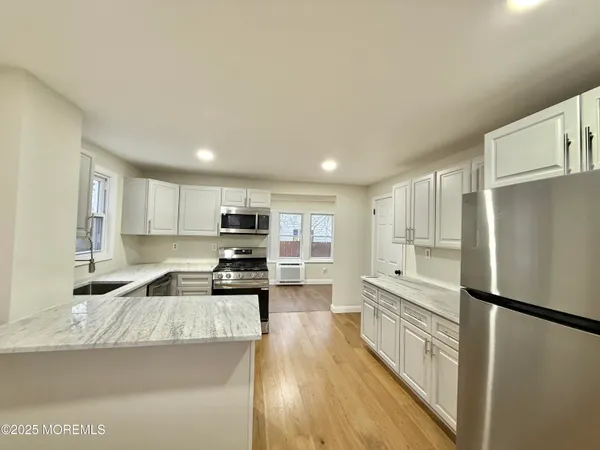 a kitchen with granite countertop a refrigerator a sink and white cabinets