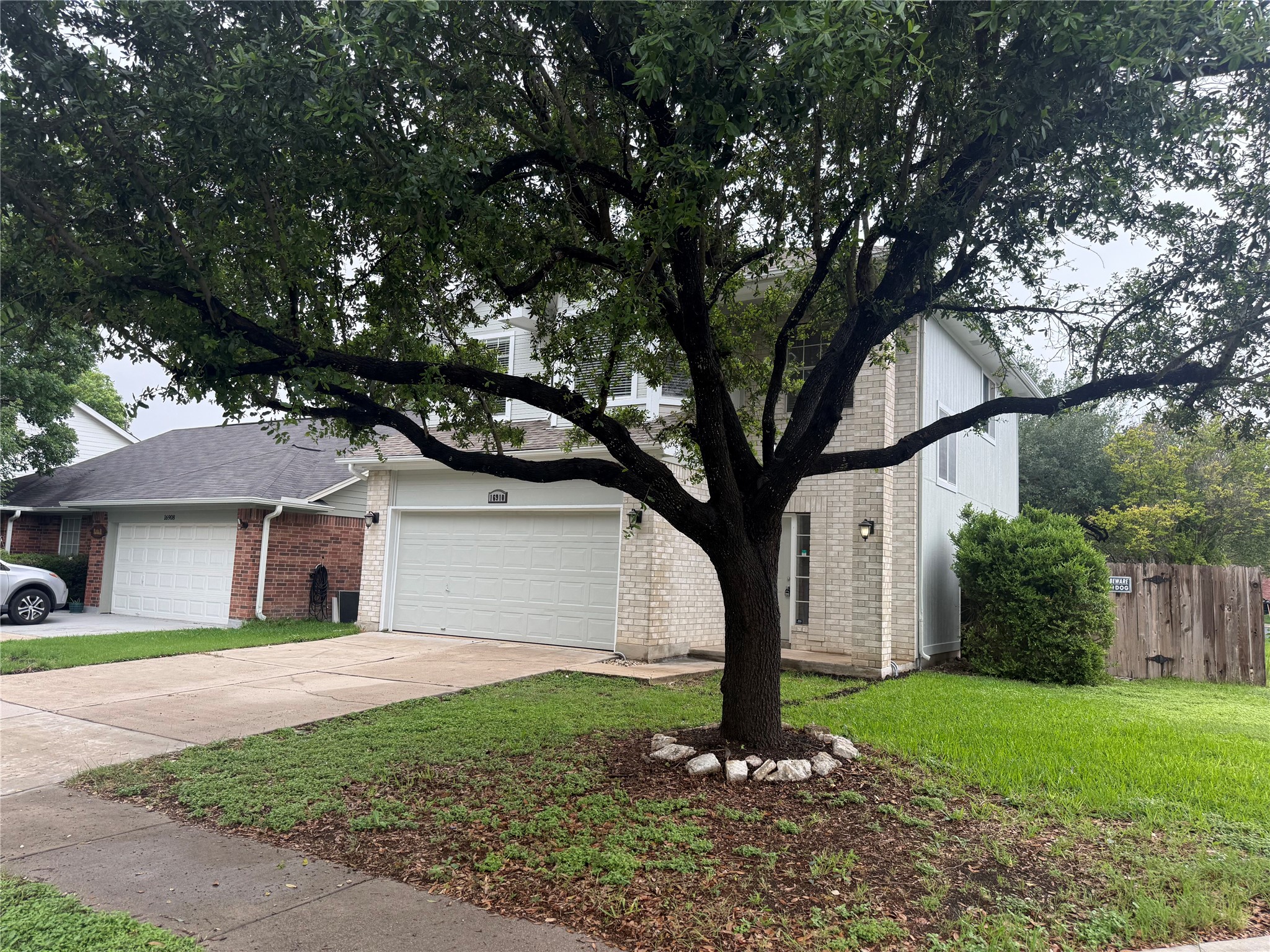 16910 Isle Of Man Road Pflugerville, TX 78660 - Photo 2 of 13 Two-story residence featuring light brick and siding exterior, a prominent mature tree, and a two-car garage