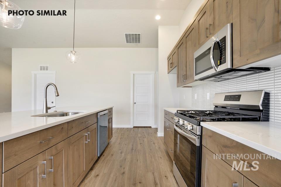 1652 Haystack Road Emmett, ID 83617 - Photo 10 of 29 Modern kitchen featuring wood-finish cabinetry, stainless steel appliances, a center island with a sink, white countertops, and wood-finish flooring