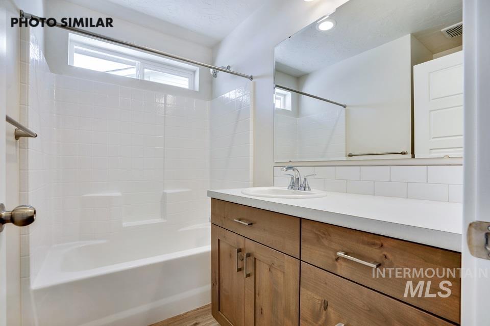 1652 Haystack Road Emmett, ID 83617 - Photo 25 of 29 Bathroom featuring a wood-finish vanity with a white countertop, an integrated sink, a large mirror, and a tiled shower/tub combination with a window
