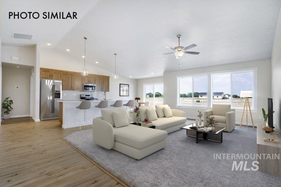 1652 Haystack Road Emmett, ID 83617 - Photo 3 of 29 Open-concept living space featuring vaulted ceilings, wood-finish flooring, a kitchen island with pendant lighting, stainless steel appliances, and large windows