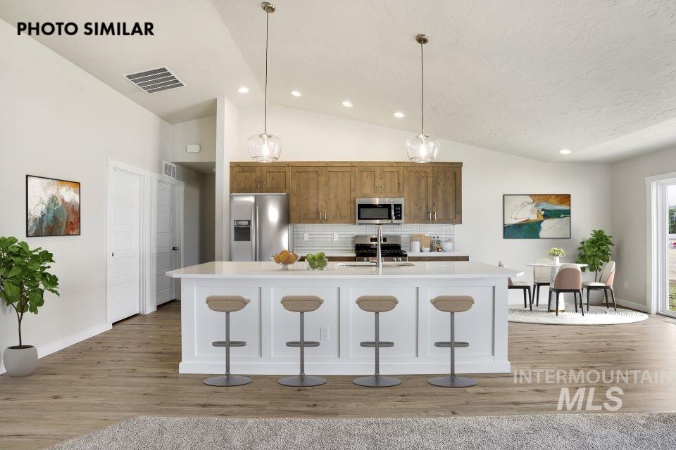 1652 Haystack Road Emmett, ID 83617 - Photo 6 of 29 Open-concept kitchen featuring an oversized island with seating, stainless steel appliances, wood-finish cabinetry, recessed lighting, and sloped ceilings