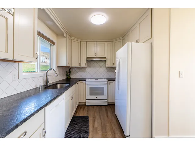 a kitchen with granite countertop a refrigerator a sink a stove and white cabinets