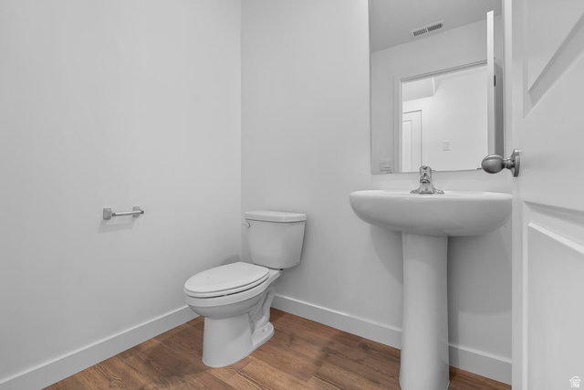 2133 Wolverine Way, Unit 2440 Washington, UT 84780 - Photo 11 of 39 Modern powder room featuring a pedestal sink with chrome faucet, a white toilet, wood-finish flooring, and a wall-mounted mirror