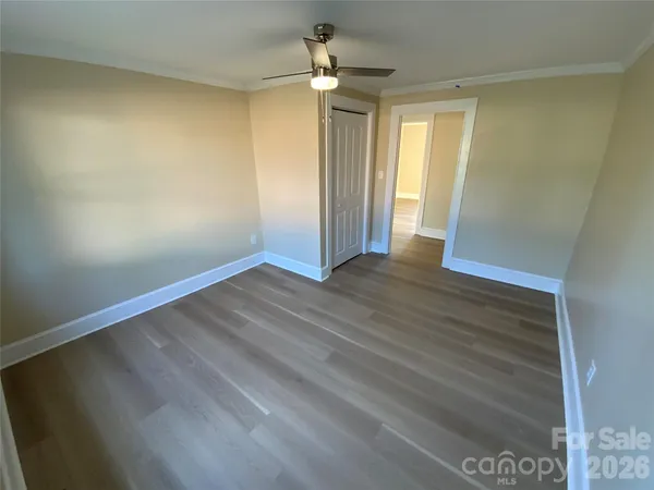 an empty room with wooden floor chandelier fan and windows