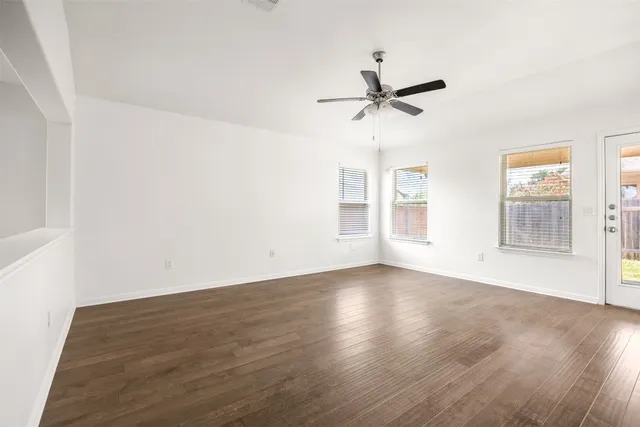 an empty room with wooden floor fan and windows