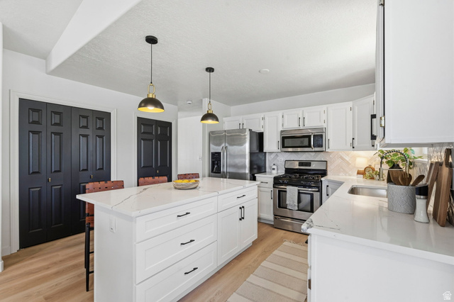 2460 Allison Way Syracuse, UT 84075 - Photo 7 of 24 Modern kitchen featuring a large central island with a solid surface countertop, white cabinetry with dark hardware, stainless steel appliances, and wood-finish flooring