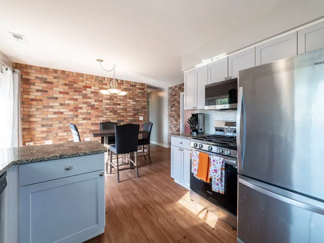 a kitchen with stainless steel appliances granite countertop a stove top oven a sink dishwasher a refrigerator and a dining table with wooden floor