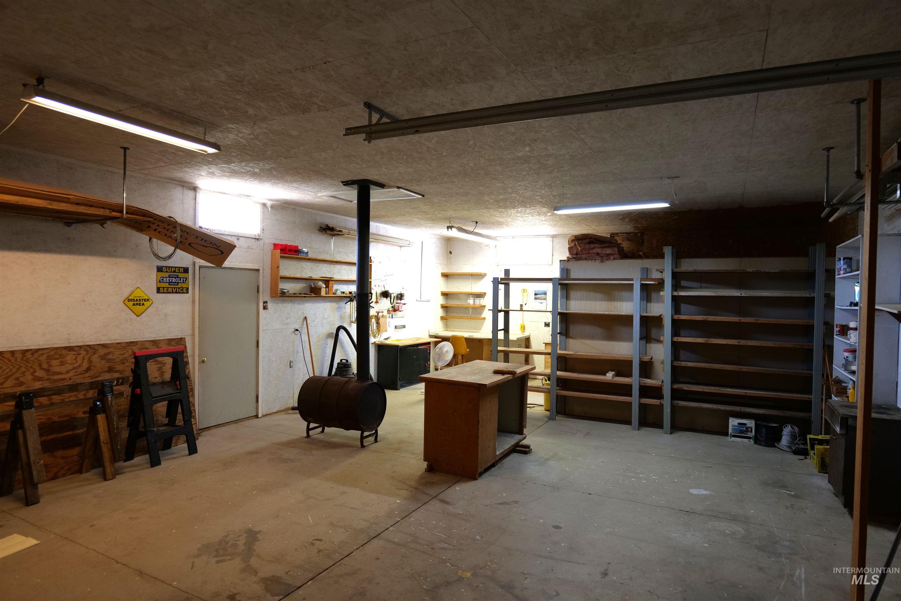 1485 East 9th Street Weiser, ID 83672 - Photo 16 of 18 Spacious shop featuring a concrete floor, built-in shelving, a drum stove, and overhead fluorescent lighting