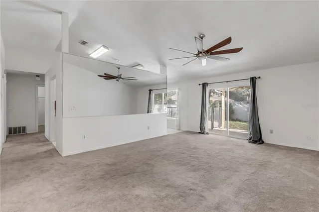 an empty room with chandelier fan and windows