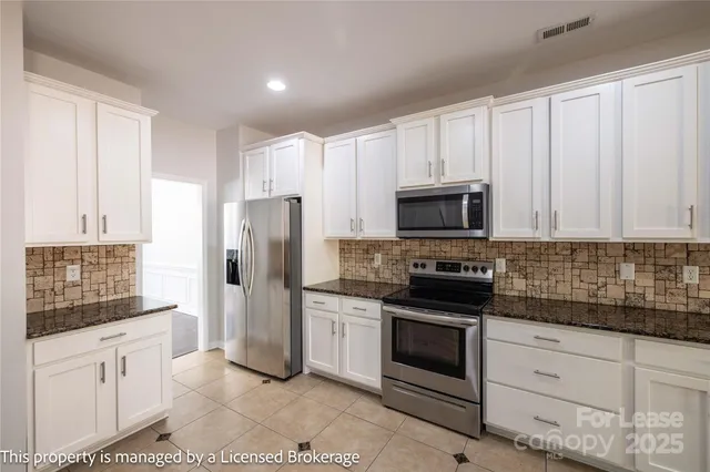 a large kitchen with granite countertop a sink white cabinets and stainless steel appliances