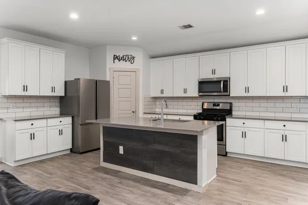 a kitchen with stainless steel appliances granite countertop a stove a sink dishwasher and a refrigerator with white cabinets